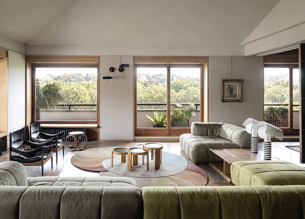 Retro-modern living room with grey and olive tufted sofas, black leather lounge chairs, a round rug with nested wood tables, and large windows framing a green Rome skyline. interior designers