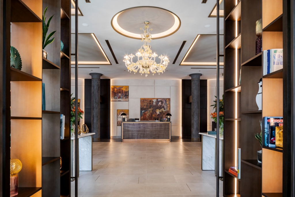 Sophisticated hotel lobby reception framed by dark wood shelving units, marble-topped consoles, a crystal chandelier, and warm accent lighting. interior designers