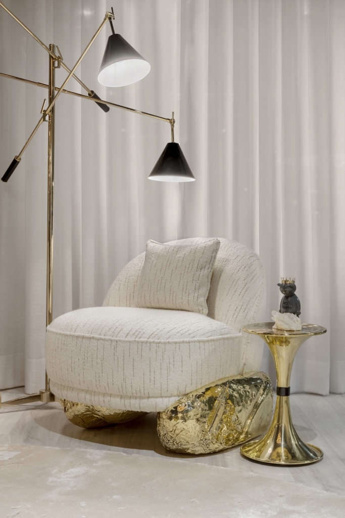 White Angra II armchair with textured upholstery and sculptural polished brass base beside a contemporary floor lamp and side table, luxury armchair.