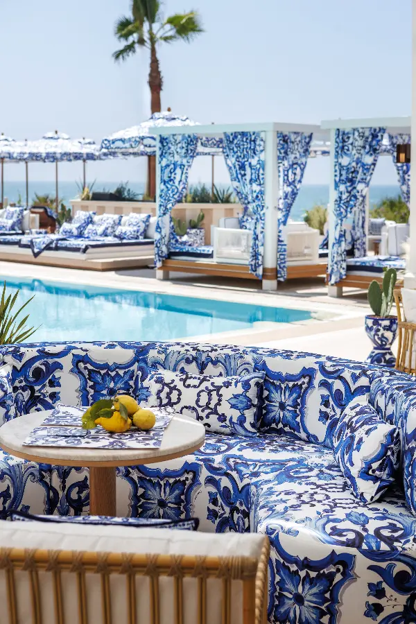Relaxed luxury showcased through Dolce&Gabbana's iconic Blu Mediterraneo patterns decorating cushions, parasols, ceramics, and bespoke outdoor furnishings.
