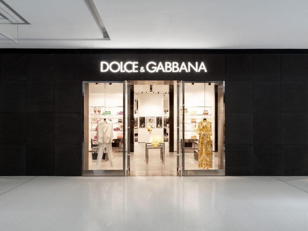 Fachada preta da loja Dolce & Gabbana com letreiro iluminado e vitrines expondo roupas e acessórios em fundo branco - lojas de luxo em São Paulo