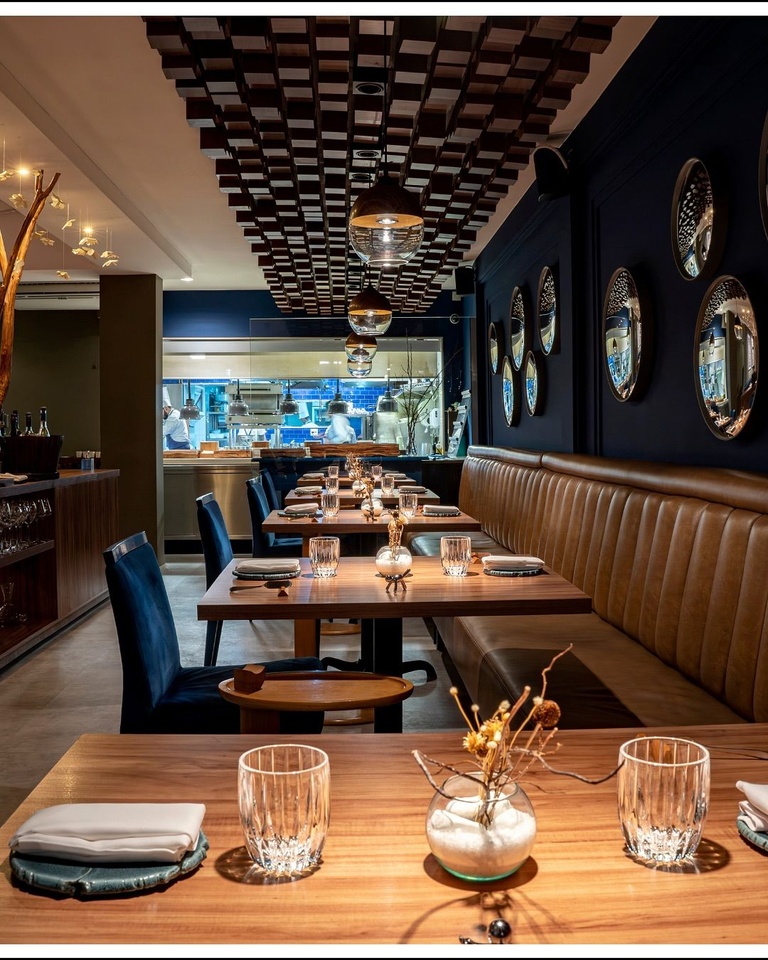 Restaurante sofisticado com teto de ripas de madeira, parede azul-marinho decorada com espelhos redondos e mesas de madeira com toalhas de linho e taças de cristal - melhores restaurantes em São Paulo