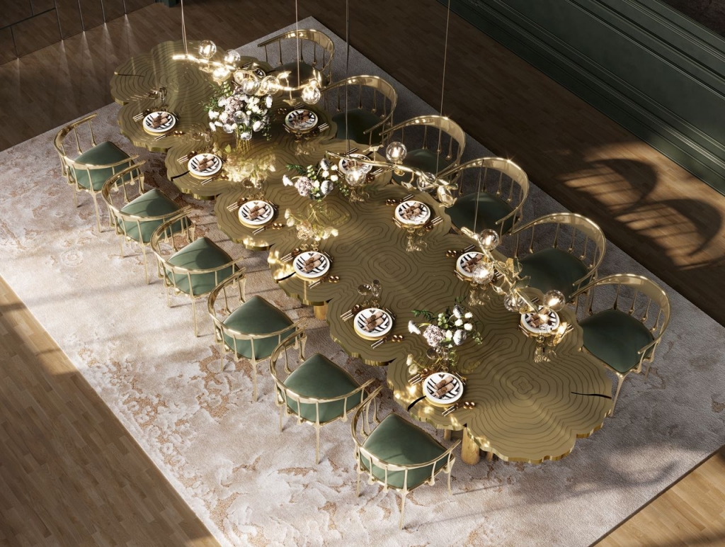 Aerial view of an organic wave-shaped gold dining table with etched tree-ring detailing, surrounded by green velvet chairs with brass frames and topped with a cascading bubble chandelier, luxury design.
