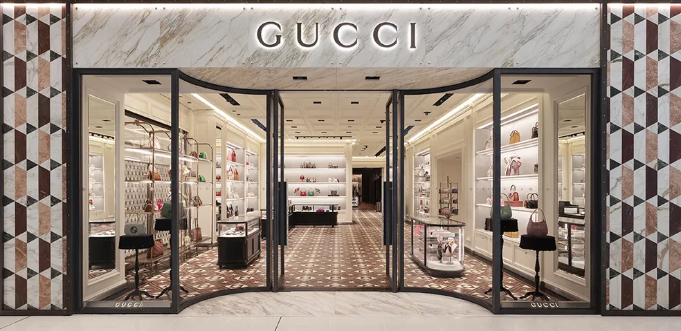 Fachada da loja Gucci com paredes de mármore geométrico, portas de vidro curvas e vitrines expondo bolsas e acessórios - lojas de luxo em São Paulo