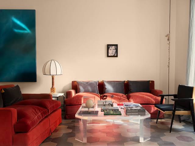 Minimalist living room with red velvet sofas, a black leather armchair, a lucite coffee table, hexagonal tiled floor, and a striking blue abstract painting. interiors designers
