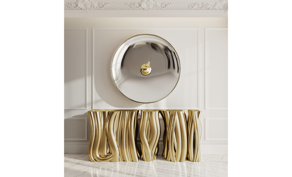Round convex mirror hanging above a gold console table with rippling, fluted column legs, luxury design.
