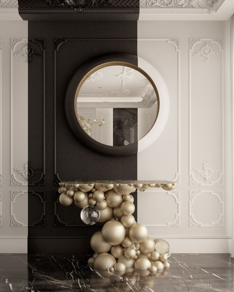 Round mirror set above a sculptural console table made of stacked spherical gold and glass orbs, against a two-tone black and cream paneled wall with marble flooring, luxury design.