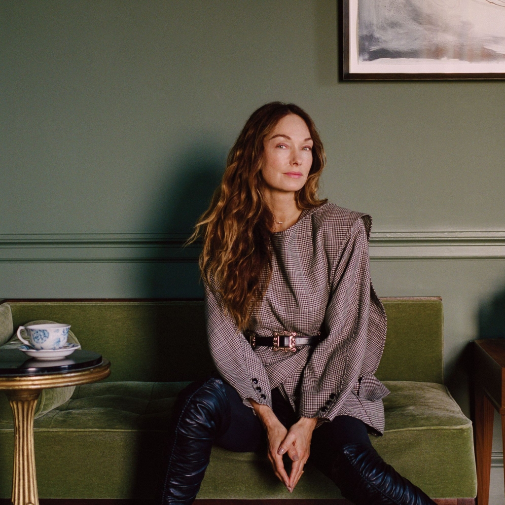 Designer Kelly Wearstler seated on a velvet sofa against a sage green wall at LA Proper Hotel.