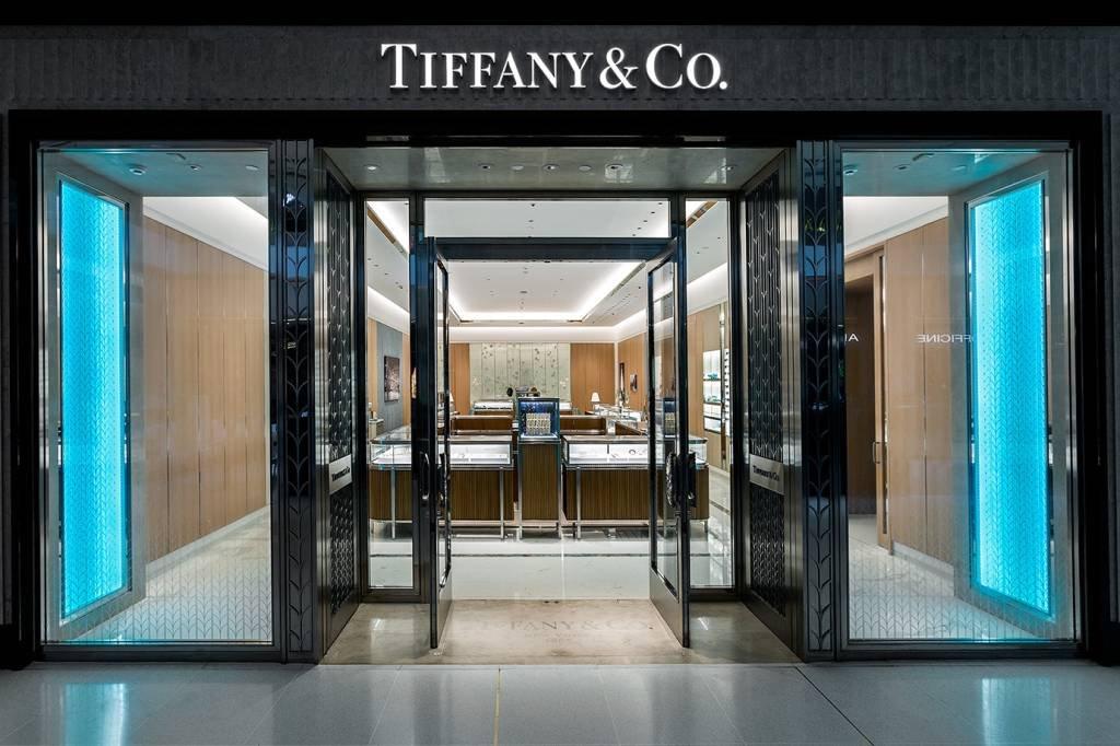 Entrada da loja Tiffany & Co. com portas de vidro emolduradas em azul-turquesa iluminado e balcões de joalheria ao fundo - lojas de luxo em São Paulo
