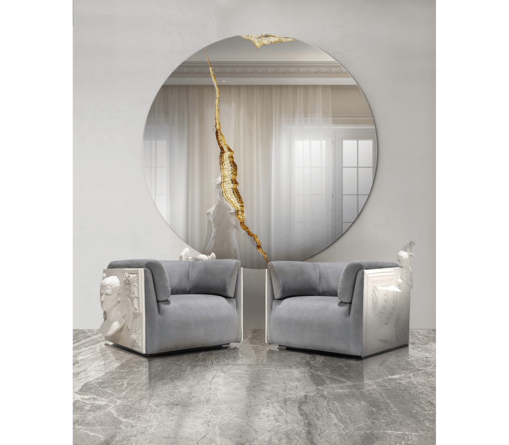 Pair of grey Versailles armchairs with sculptural carved side panels positioned beneath a round statement mirror with a gold accent, luxury armchair.