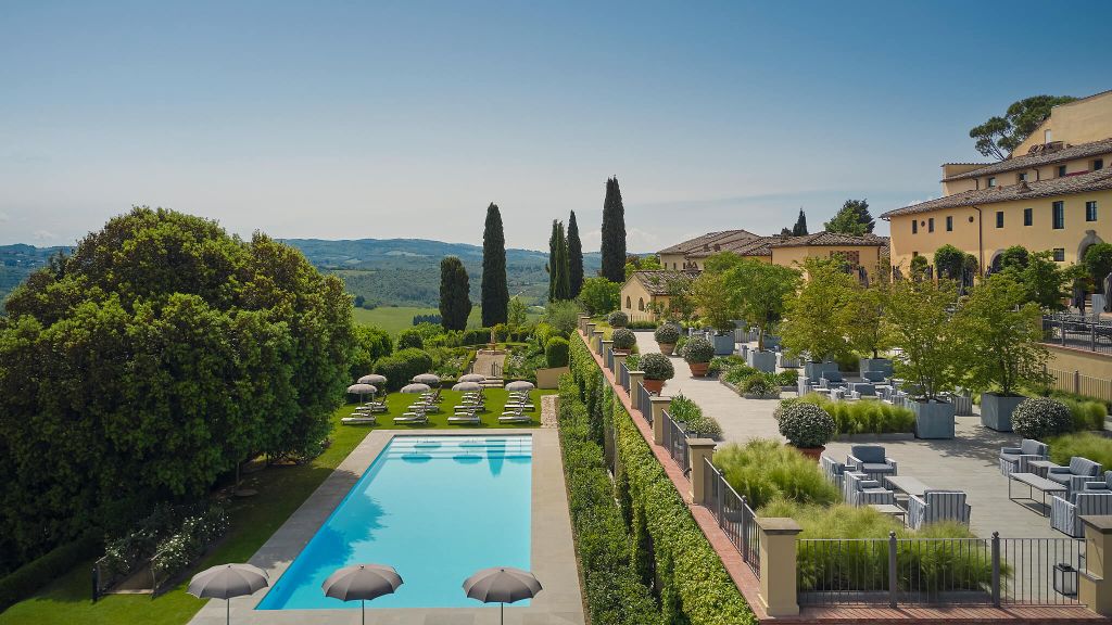 Countryside resort pool area with a wide terrace, sun loungers, and distant green hills. Old Money Hotels in Italy