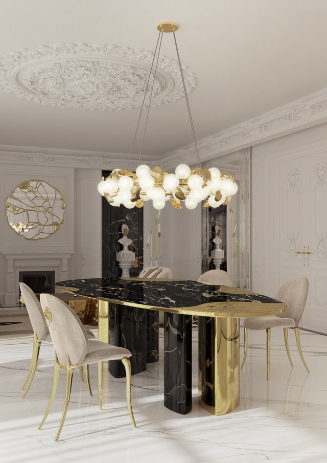 Oval black marble table with polished gold column legs under a gold sphere chandelier -luxury dining table