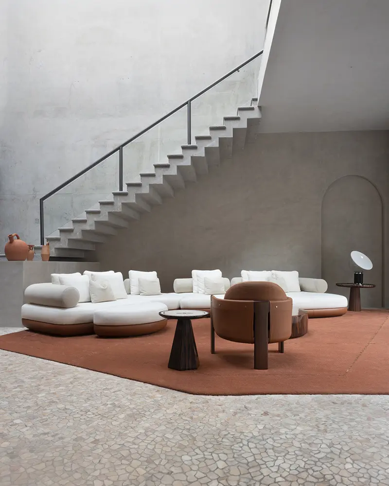Sunken lounge area with white modular sofas, a terracotta rug, and a curved staircase overhead -top showrooms in São Paulo