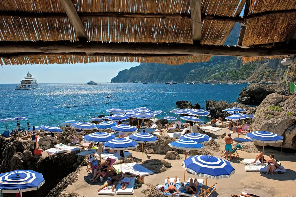 Blue-and-white striped umbrellas on a rocky platform overlooking the sea -luxury beach clubs in Europe