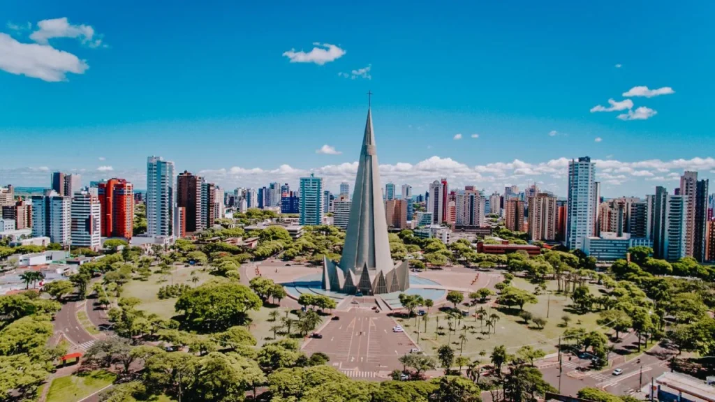 Modern spire-shaped church surrounded by gardens and the city skyline under a blue sky -top places to live in São Paulo