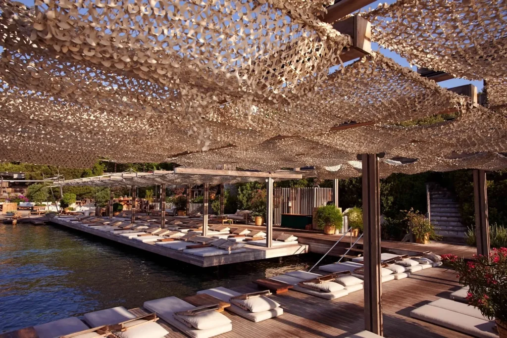 Deck covered by a decorative net canopy with loungers over the water -luxury beach clubs in Europe