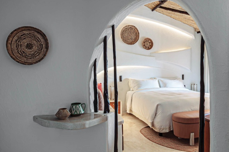 Archway leading into a whitewashed bedroom with woven wall baskets and a thatched ceiling