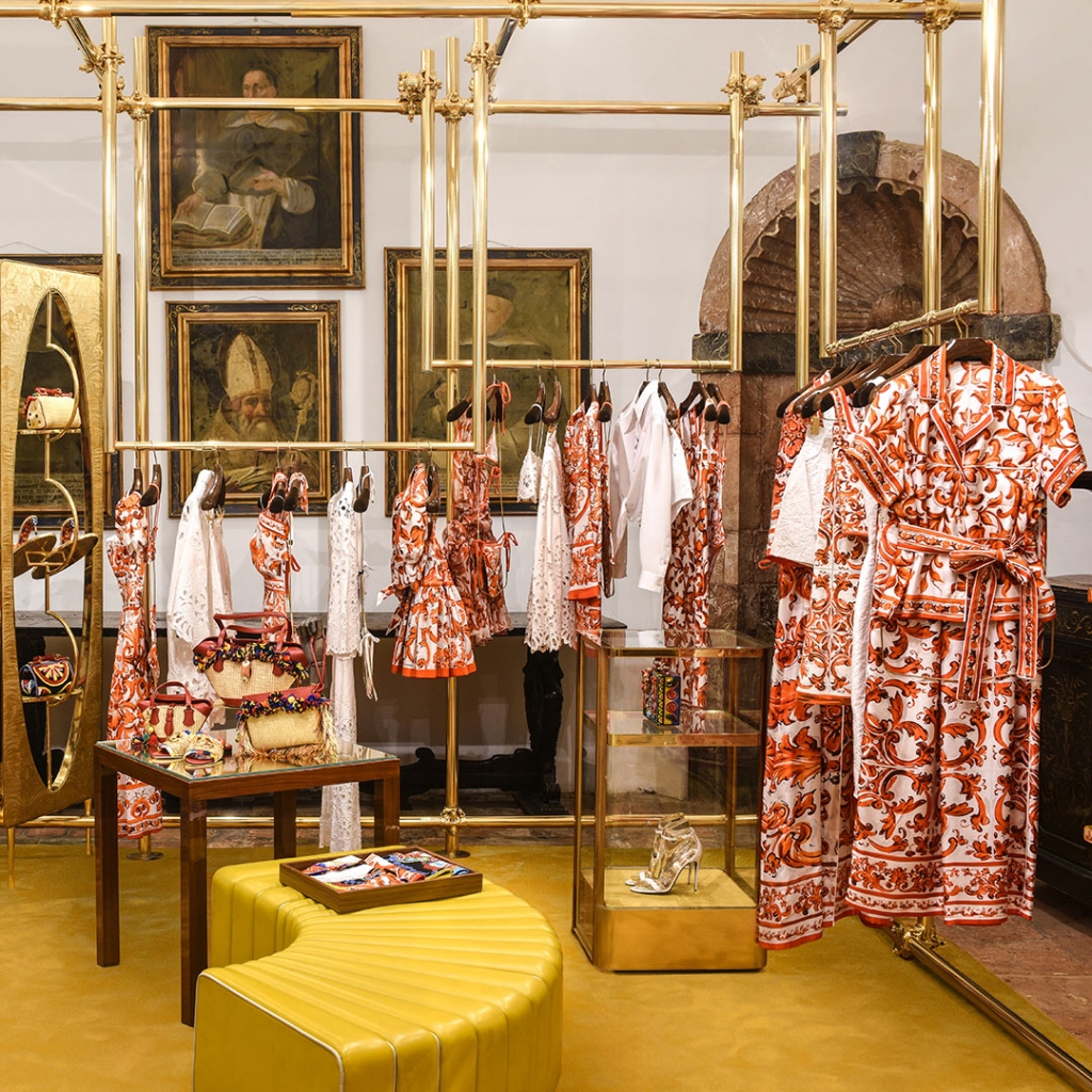 Boutique display of orange and white printed dresses and accessories on gold racks against a backdrop of framed portraits -four seasons hotel taormina