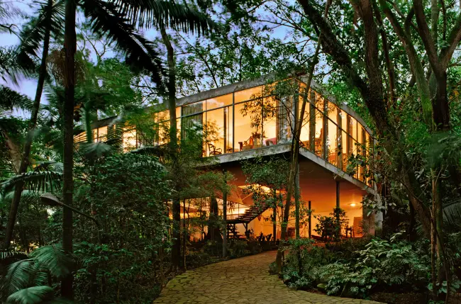 Modern glass house suspended among tropical trees, lit up at nightfall -top places to live in São Paulo