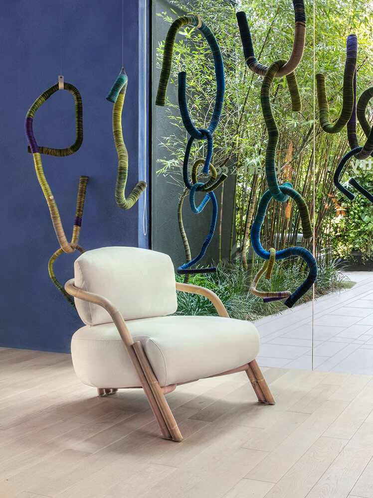Cream upholstered lounge chair with wooden frame beside colorful woven sculptural hanging decor -top showrooms in São Paulo