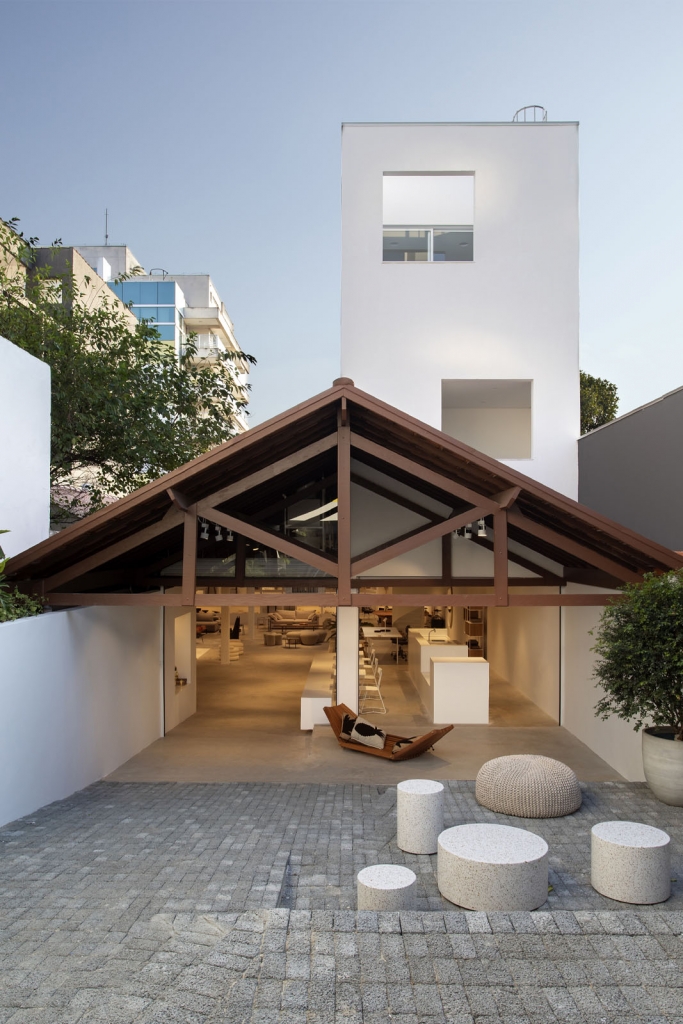 Exterior view of showroom with a large exposed timber gable roof structure opening onto a stone courtyard -showrooms in Brazil
