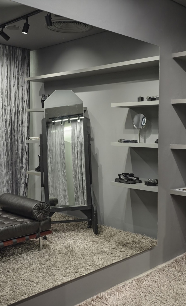 Fitting room nook with a freestanding mirror, leather daybed, and shelves displaying shoes and accessories -top showrooms in São Paulo