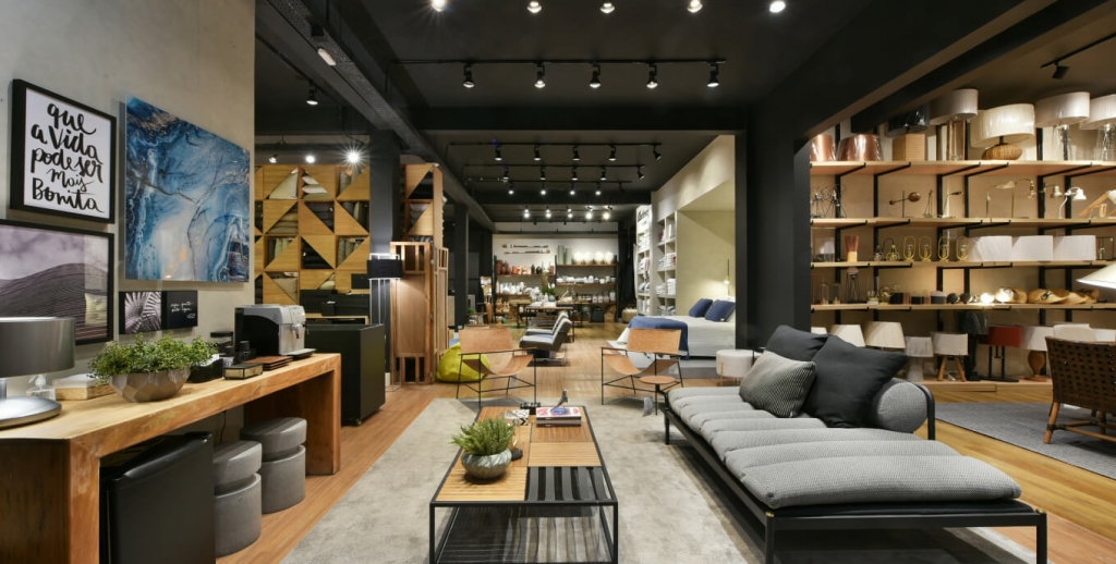 Home decor showroom interior with a grey sofa, wall shelving of lamps, and a mixed seating display area -top showrooms in São Paulo