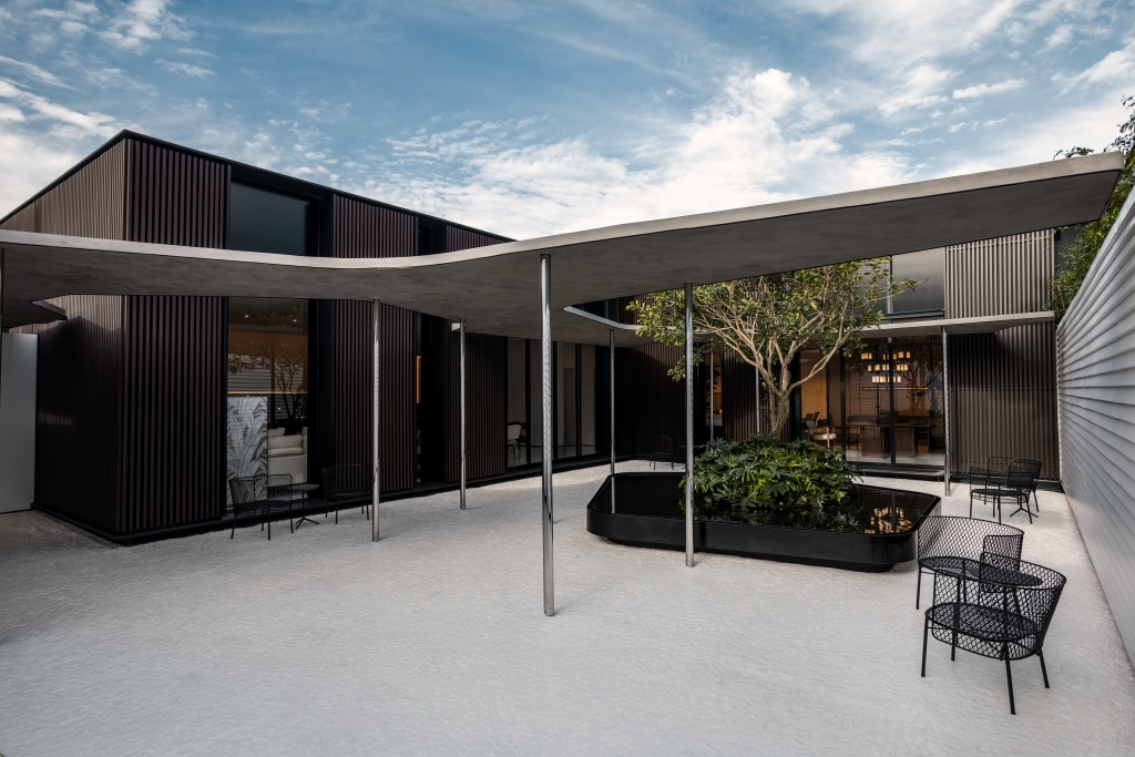 Modern courtyard with dark slatted facade, a sweeping concrete canopy on slim columns, and a central planted water feature -showrooms in Brazil