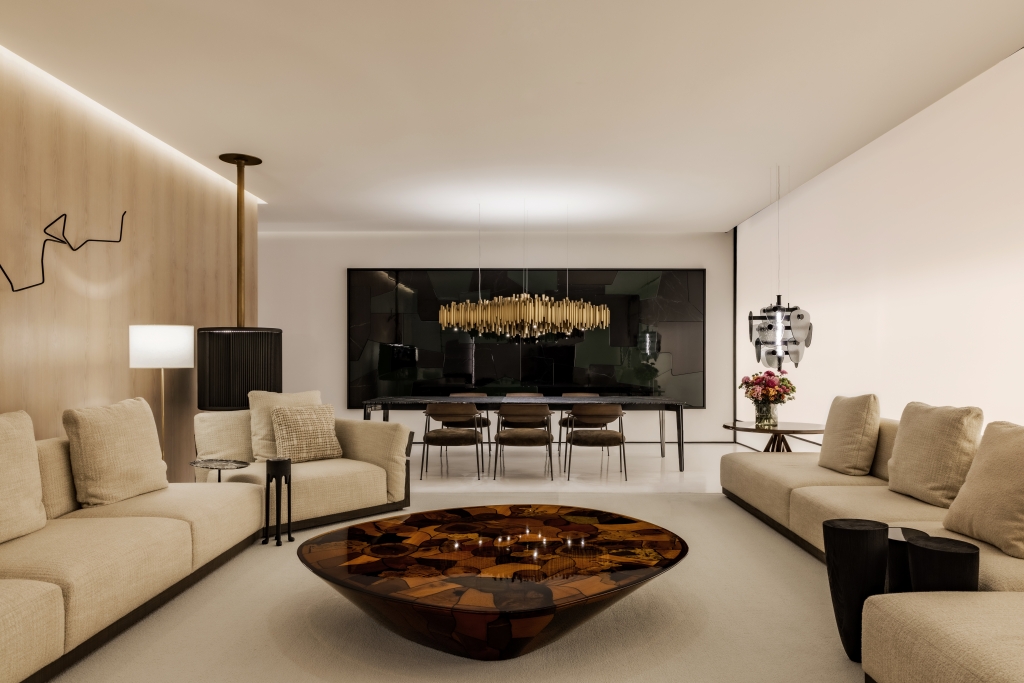 Elegant living and dining space with beige sofas, a sculptural resin coffee table, brass tube chandelier, and wood-paneled wall -showrooms in Brazil