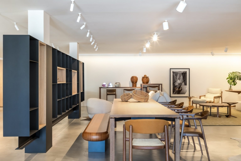 Showroom space with a modular black shelving unit, a wooden dining table, and an assortment of chairs in a minimalist setting -showrooms in Brazil