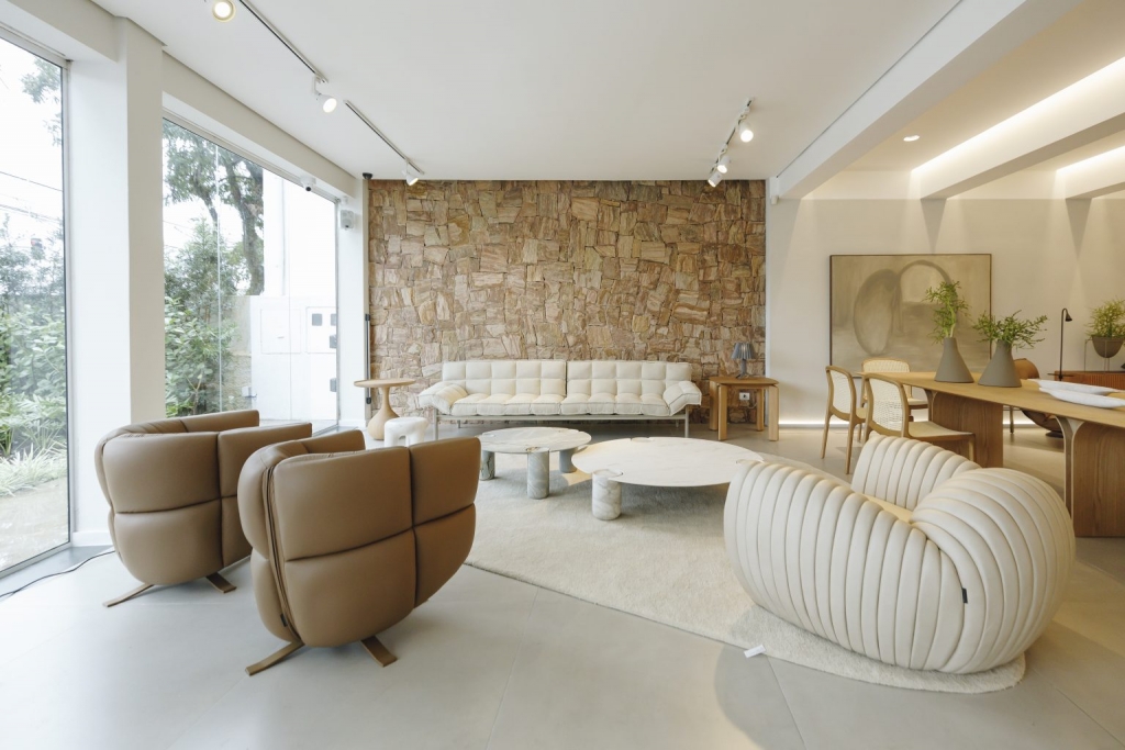 Showroom lounge with a natural stone feature wall, camel leather armchairs, and an organic-shaped white sofa -showrooms in Brazil