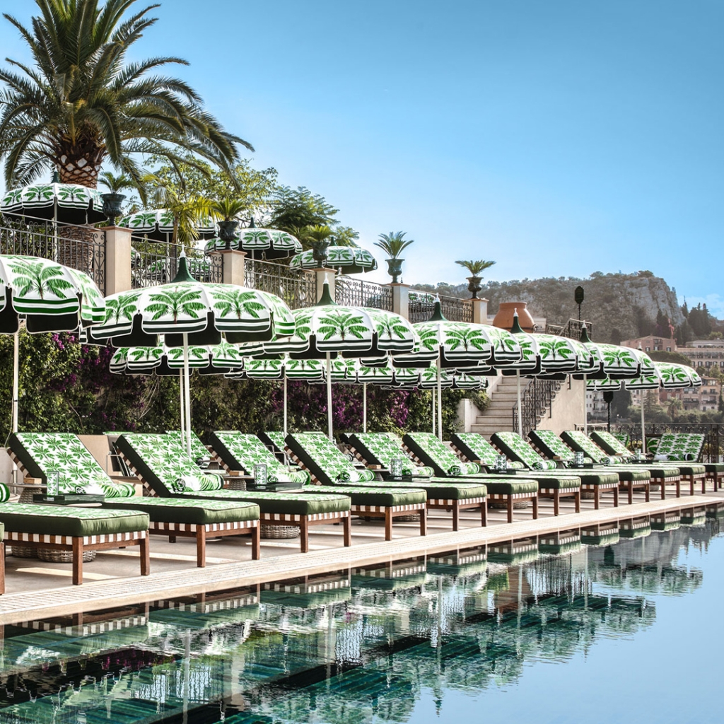 Poolside deck lined with green and white palm-print sun loungers and umbrellas overlooking a mountain view -four seasons hotel taormina