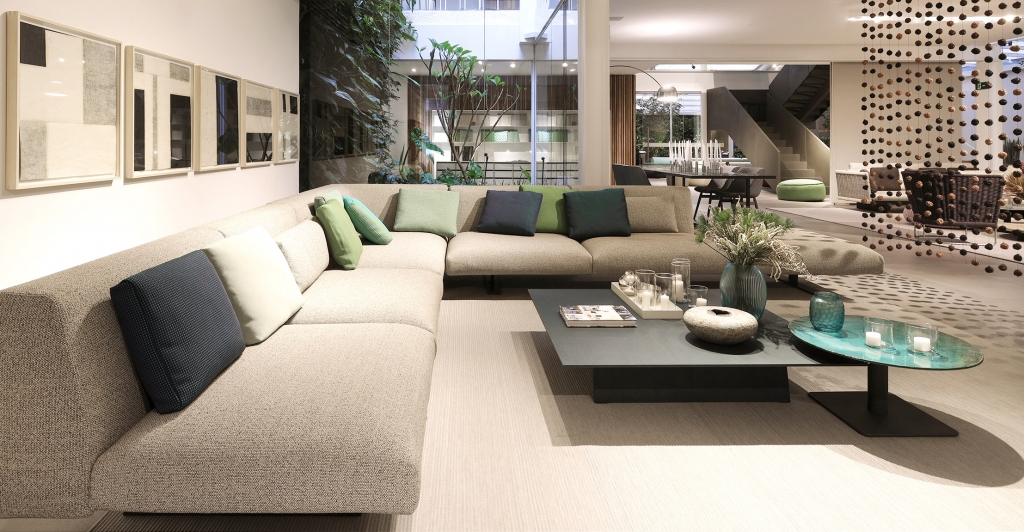 Open-plan lounge with a beige sectional sofa, green and blue cushions, and a decorative beaded room divider -top showrooms in São Paulo