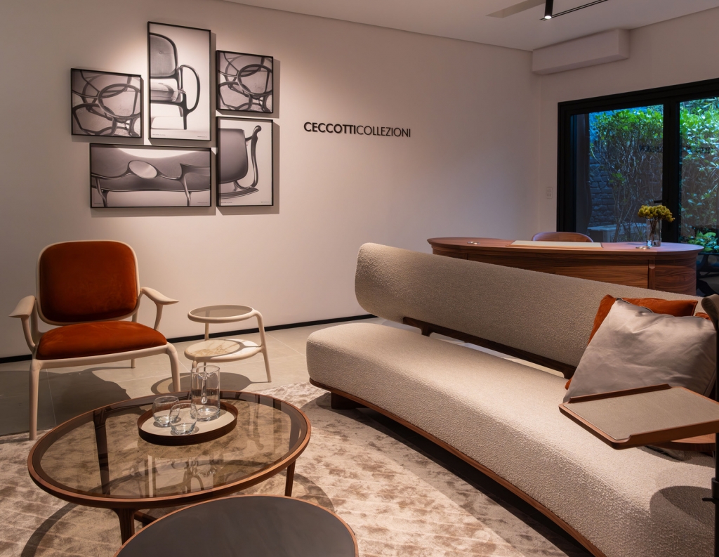 Ceccotti Collezioni showroom corner with a rust-orange armchair, curved bouclé sofa, and framed furniture sketches -top showrooms in São Paulo