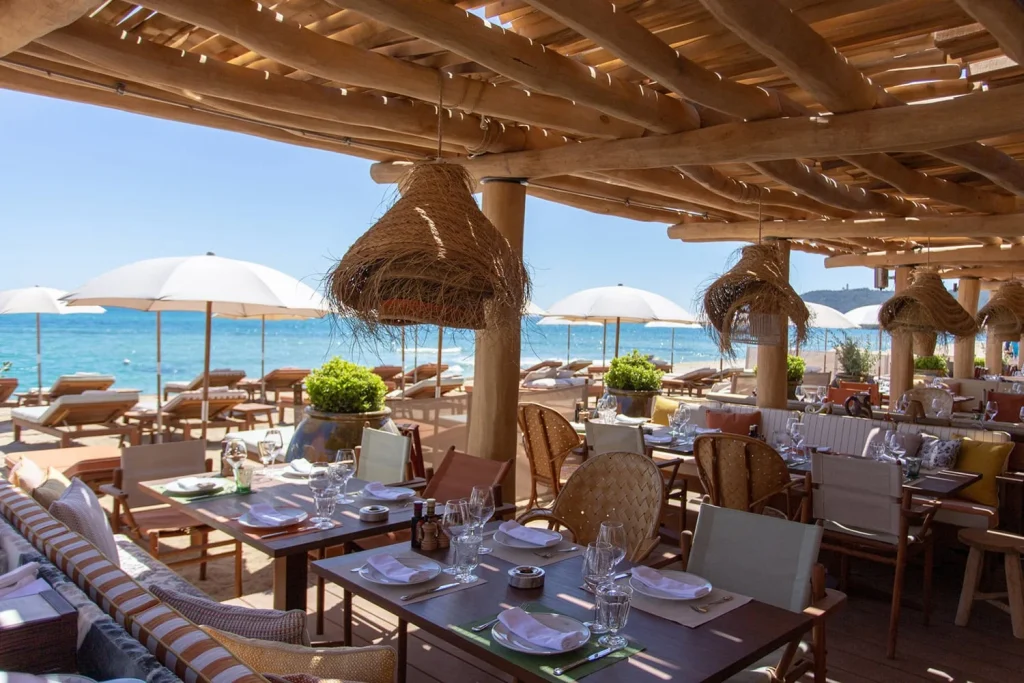 Dining area under a wooden pergola with sea views and white umbrellas -luxury beach clubs in Europe