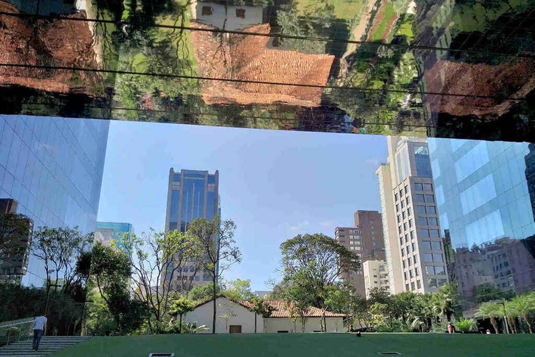 Glass facade reflection showing modern buildings, an old house with a tiled roof, and a pedestrian walking -top places to live in São Paulo