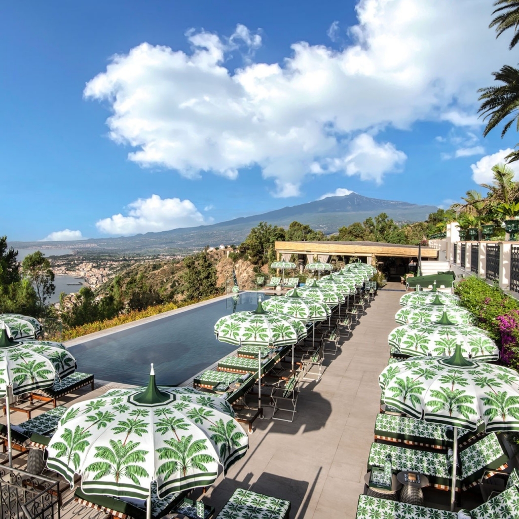 Elevated view of a poolside terrace lined with palm-print umbrellas and loungers overlooking the sea and Mount Etna -four seasons hotel taormina