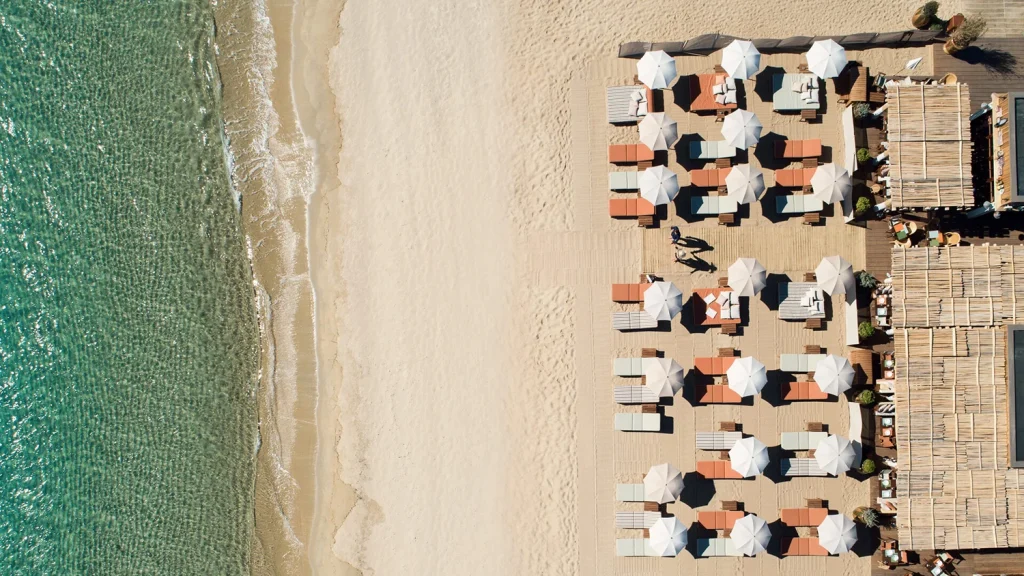 Aerial view of a beach club with loungers and umbrellas beside turquoise water -luxury beach clubs in Europe