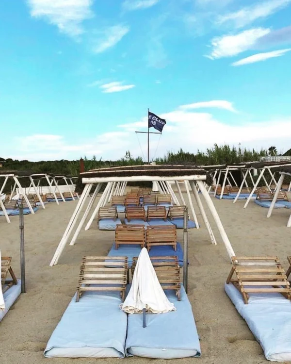 Row of white sun loungers at a beach club with a flag in the background -luxury beach clubs in Europe