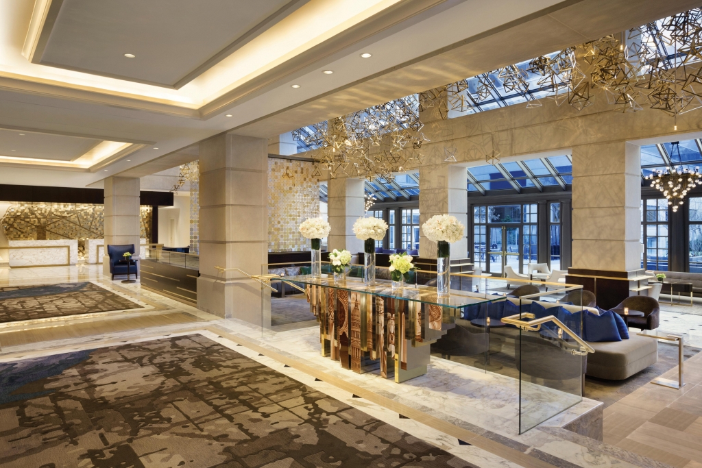 Detailed view of a decorative console table with intricate, illustrated base panels and abstract gold sculptures, situated under a skylight - Fairmont Hotel.