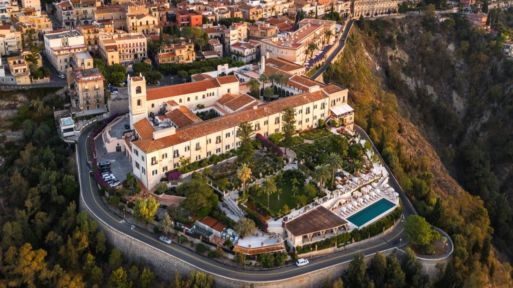 Aerial view of a historic clifftop hotel with landscaped gardens, a swimming pool, and terracotta rooftops overlooking the town -four seasons hotel taormina