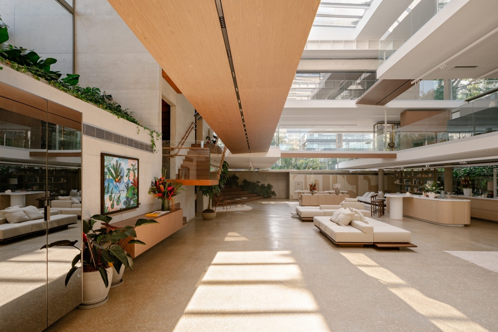 Expansive double-height atrium interior with a suspended wooden staircase, beige sofas, and natural skylight -showrooms in Brazil