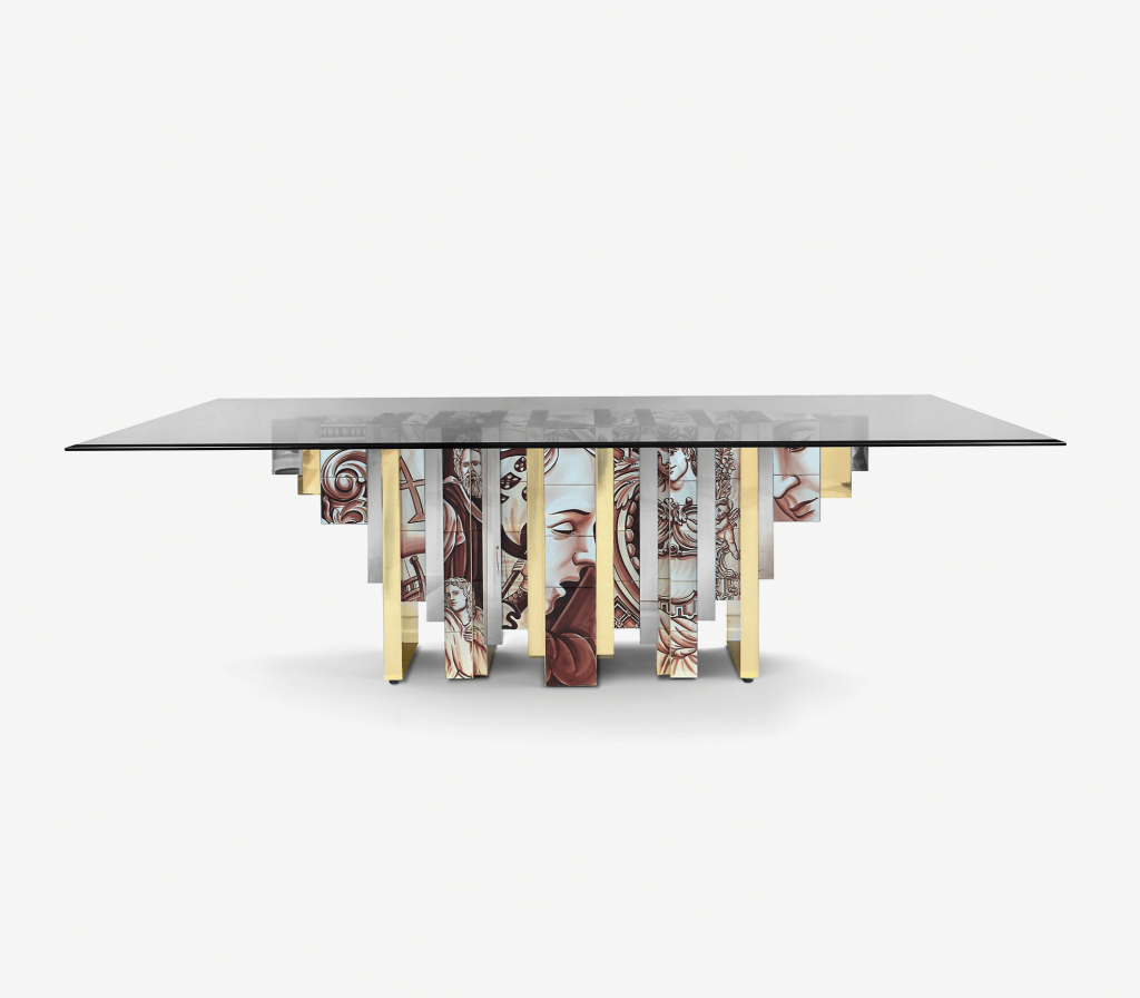 A table with a glass top and a highly detailed, artistic base featuring classical European illustrations in gold and sepia tones - Fairmont Hotel.