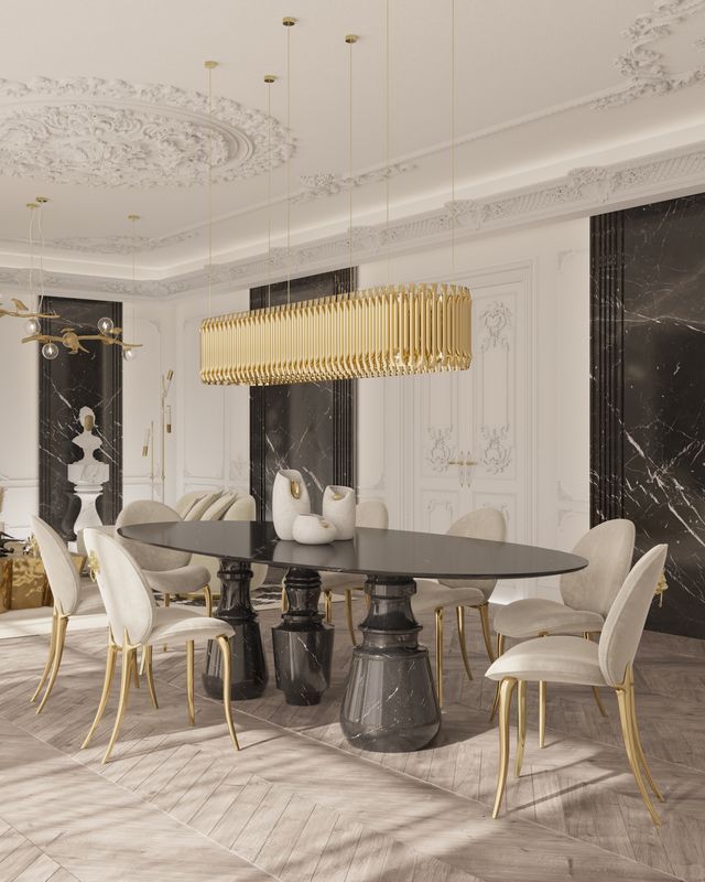 Oval black marble table with sculptural column legs beneath a linear gold chandelier -luxury dining table
