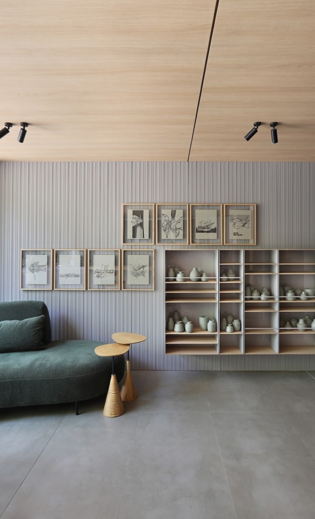 Wall display of framed sketches and ceramic vessels on wooden shelving beside a green chaise sofa -top showrooms in São Paulo