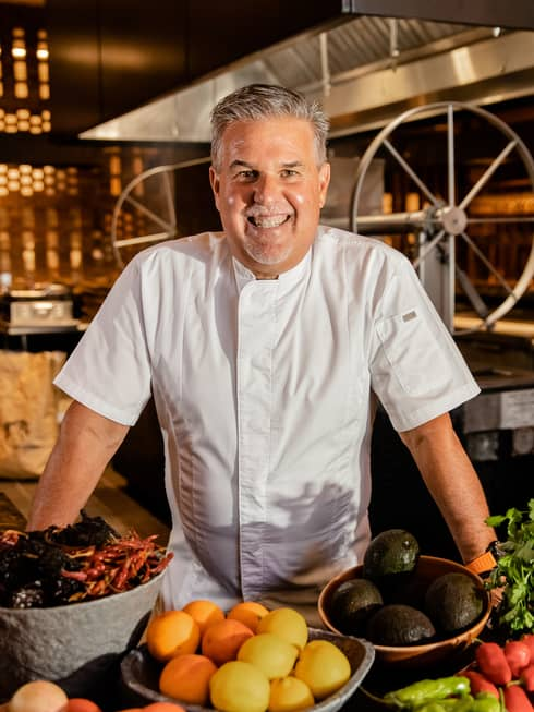 Chef smiling in the kitchen with fresh ingredients at Four Seasons Los Cabos