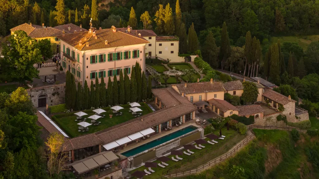 High-angle view of a Tuscan estate with a long swimming pool and cypress trees. Old Money Hotels in Italy