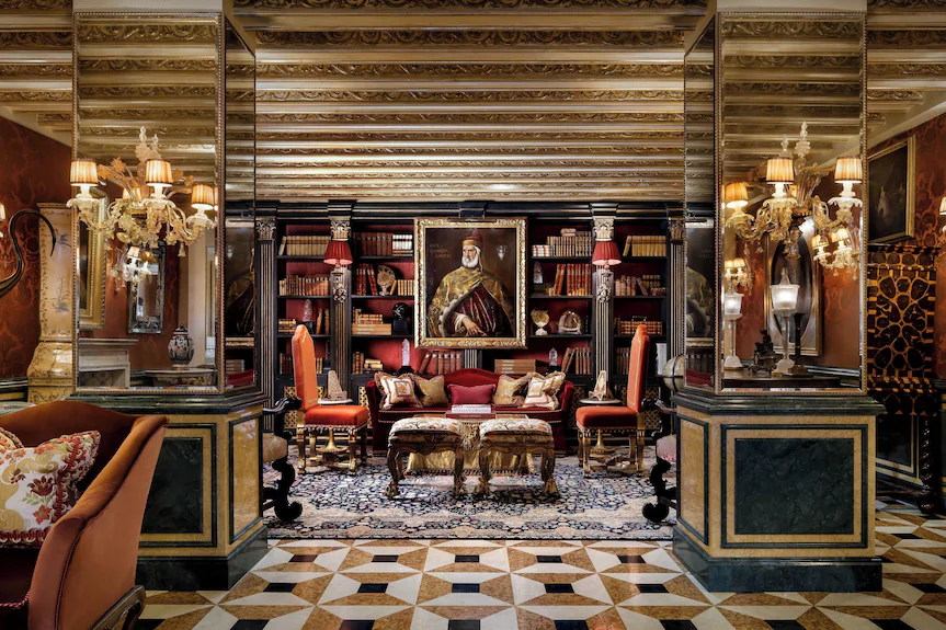 Opulent room with wood-paneled bookshelves, mirrored pillars, and classical portraits. Old Money Hotels in Italy
