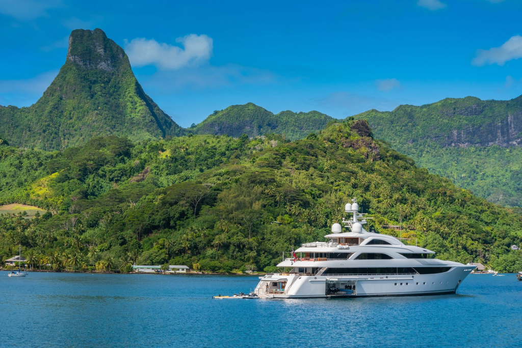 Yacht Destinations — luxury yacht sailing across the Mediterranean Sea with lush green mountains rising along the coastline in the background