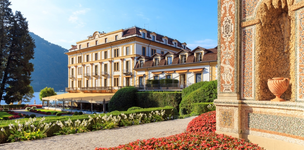 Grand yellow and white villa surrounded by manicured gardens next to a lake. Old Money Hotels in Italy